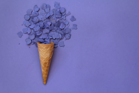 Top view of ice cream cone with purple confetti on purple background with copy space