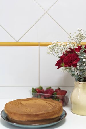Homemade cake on kitchen table with strawberries and red flowers on the backgroundの写真素材