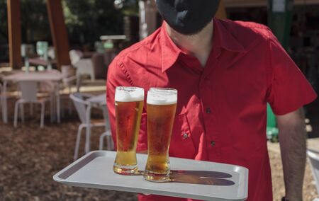Waiter with protective mask on face holding tray with beersの写真素材