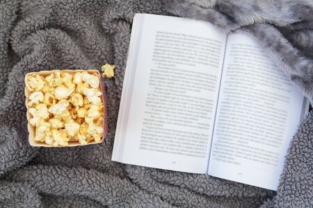 Top view of popcorn box and open book on warm blanketの写真素材