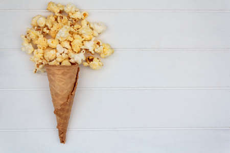 Top view of ice cream cone with popcorns on white wooden table with copy spaceの写真素材