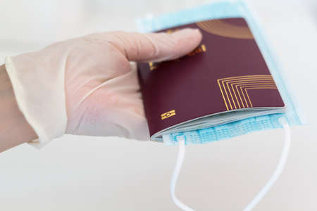 Hand with glove holding passport and medical mask. Traveling during coronavirus, covid-19 pandemicの写真素材