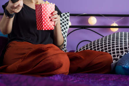 Woman sitting on bed holding box of popcornの写真素材