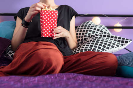 Woman eating popcorn in bedの写真素材