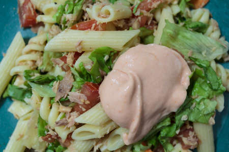 Pasta salad with lettuce, tuna, tomato, and sauce on topの写真素材