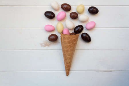 Top view of ice cream cone with sweet almond eggs on white wooden tableの写真素材