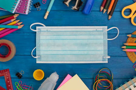 Top view of school supplies and covid-19 mask on blue wooden tableの写真素材
