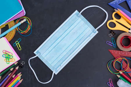 Top view of School supplies and protective face mask on chalkboard. Back to school during covid-19 pandemic, new normal conceptの写真素材