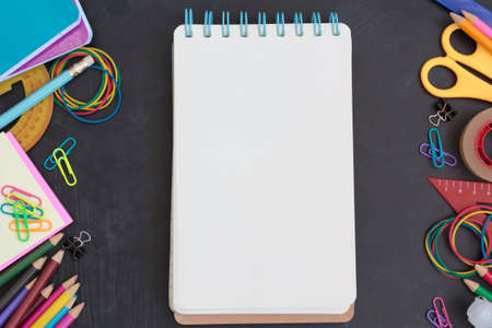 School supplies and notepad with blank page on chalkboard. Top view with copy space. Back to school conceptの写真素材
