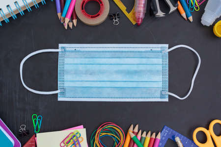 School supplies and protective face mask on chalkboard. Back to school during covid-19 pandemic, new normal conceptの写真素材