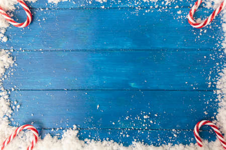 Top view of snow frame and candy cane on blue wooden table with copy space for background useの写真素材