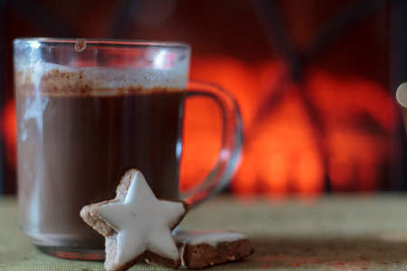 Cup of hot chocolate and cookie with fireplace on the background. Winter, cold days and comfort conceptの写真素材