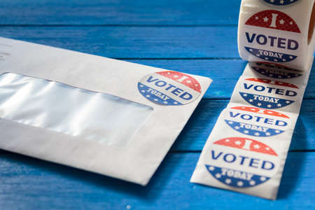 Envelope with voting ballot papers sent by mail for absentee vote in presidential election and I Voted today stickers on blue wooden tableの写真素材