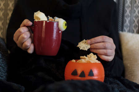 Woman at sofa eating halloween treats and drinking spooky drinkの写真素材