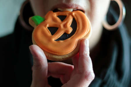 Close-up of woman eating a halloween pumpkin biscuitの写真素材