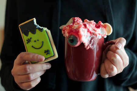 Woman holding monster halloween cookie missing a bite and scary halloween beverageの写真素材