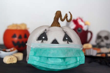 Pumpkin with protective face mask on table with treats and snacks. Celebrating halloween at home during covid-19 pandemicの写真素材