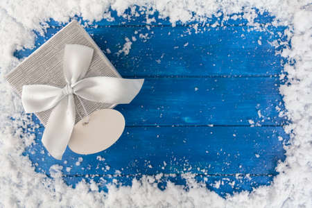 Christmas background with gift box and blank card on blue wooden table with snow. Top view with copy spaceの写真素材