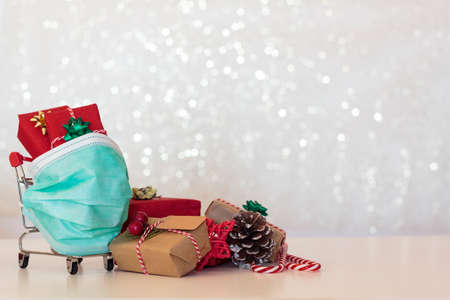 Shopping cart with Christmas gifts and presents and protective face mask. Concept of Christmas during covid-19 pandemicの写真素材