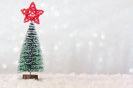 Christmas tree with red star on top on snowy background. Sparkle bokeh background with copy space