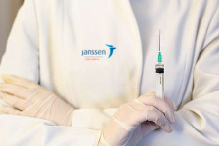 Lisbon, Portugal - November 22, 2020: Medic ,scientist, pharmacist holding Syringe with Janssen logo on lab coat. Coronavirus, Covid-19 vaccine conceptのeditorial素材