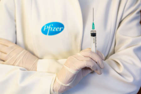 Lisbon, Portugal - November 22, 2020: Medic ,scientist, pharmacist holding Syringe with Pfizer logo on lab coat. Coronavirus, Covid-19 vaccine conceptのeditorial素材