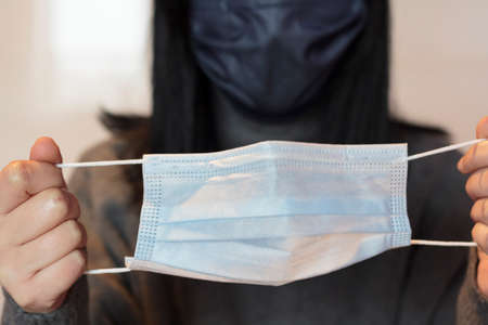 Woman using protective face mask and holding a second mask to useの写真素材
