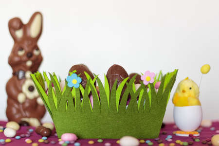 Easter basket with chocolate eggs, decorative chick, chocolate bunny and almonds on table. Easter holiday decorationの写真素材