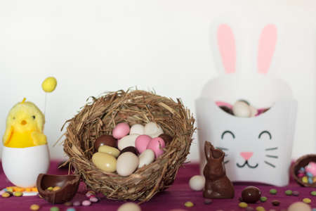 Bird nest with easter almond eggs, chocolate bunny missing a bite, treat box with almods and decorative chickの写真素材