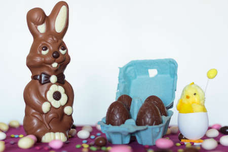 Chocolate bunny, egg carton with chocolate eggs and decorative chick against white backgroundの写真素材