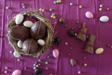 Top view of nest with chocolate eggs, chocolate rabbits and easter almonds on tableの写真素材