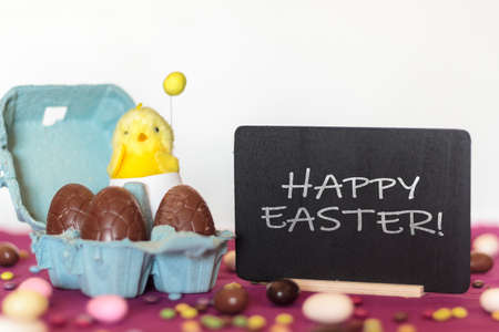 Egg carton with chocolate eggs and chick with Happy Easter blackboardの写真素材