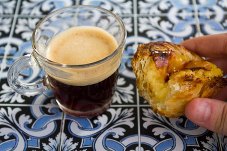 Hand holding a portuguese custard tart called pastel de nata, with black espresso coffee
