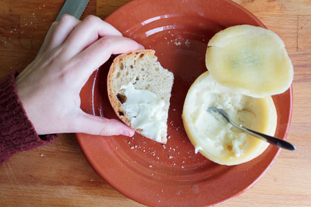 Top view of woman hand taking a slice of bread with delicious soft and creamy cheese