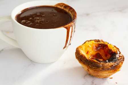 White cup with hot chocolate and custard tart on tableの写真素材