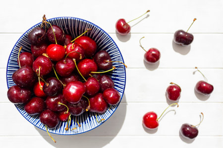 Top view of bowl with fresh cherries on white wooden table