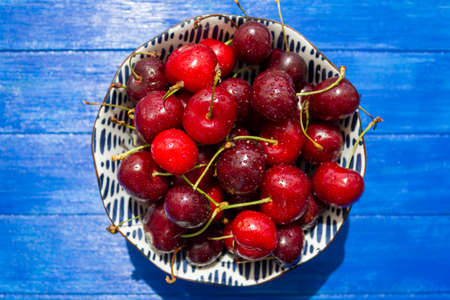 Top view fresh cherries bowl with water drops on blue wooden tableの写真素材