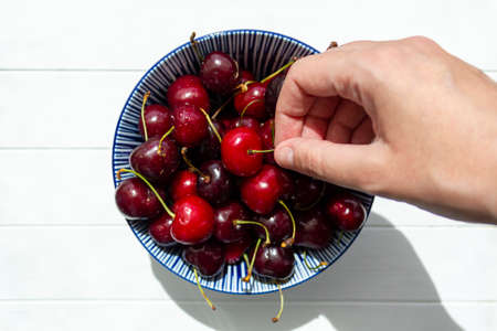 Hand picking a cherry from bowl of cherriesの写真素材