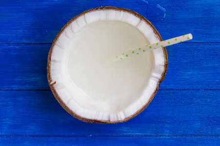 Cracked coconut with coconut water and straw on blue wooden tableの写真素材