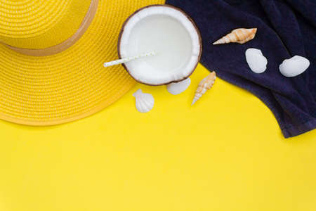 Top view of summer hat, beach towel, shells and coconut with straw on yellow background with copy spaceの写真素材
