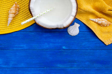 Top view of summer hat, beach towel, shells and coconut with straw on blue wooden table with copy spaceの写真素材