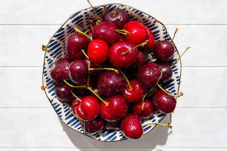 Top view of bowl with fresh and delicious cherries on white wooden tableの写真素材