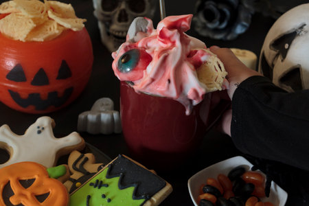 Woman holding mug with delicious halloween drink on decorated table with candy and snacksの写真素材