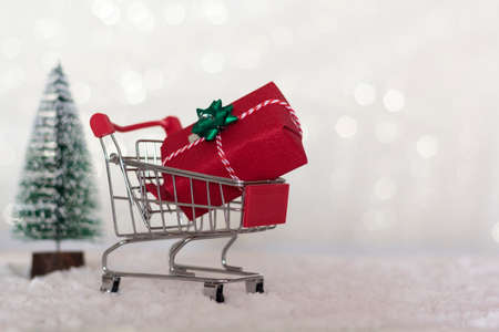 Shopping cart with christmas gift and christmas tree on snowy background with copy spaceの写真素材
