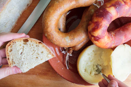 Woman hand eating cheese with slice of bread with portuguese sausages on plateの写真素材