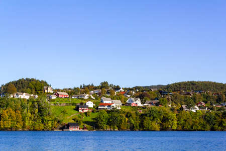 Colorful traditional Norwegian houses near the sea with green forest on mountains and blue skyの写真素材
