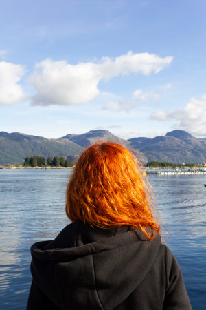 Rear view of redhead girl looking at sea and mountains landscape