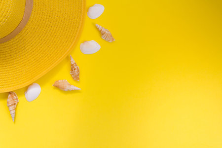 Top view of yellow straw summer hat and shells on yellow background with copy spaceの写真素材