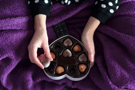 Top view of Woman with blanket eating heart chocolates from heart-shaped gift boxの写真素材
