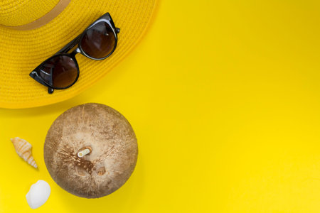 Straw summer hat, sunglasses and coconut with straw on yellow background. Top view with copy space